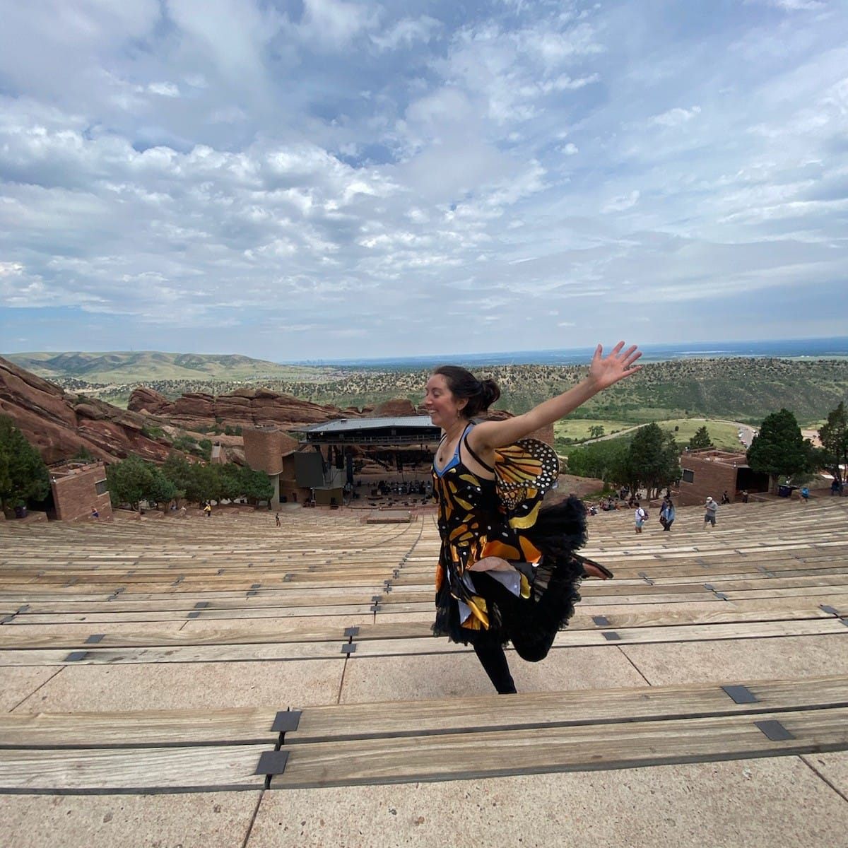 a young woman wearing a butterfly costume jumps for joy at red rocks amphitheater in Colorado