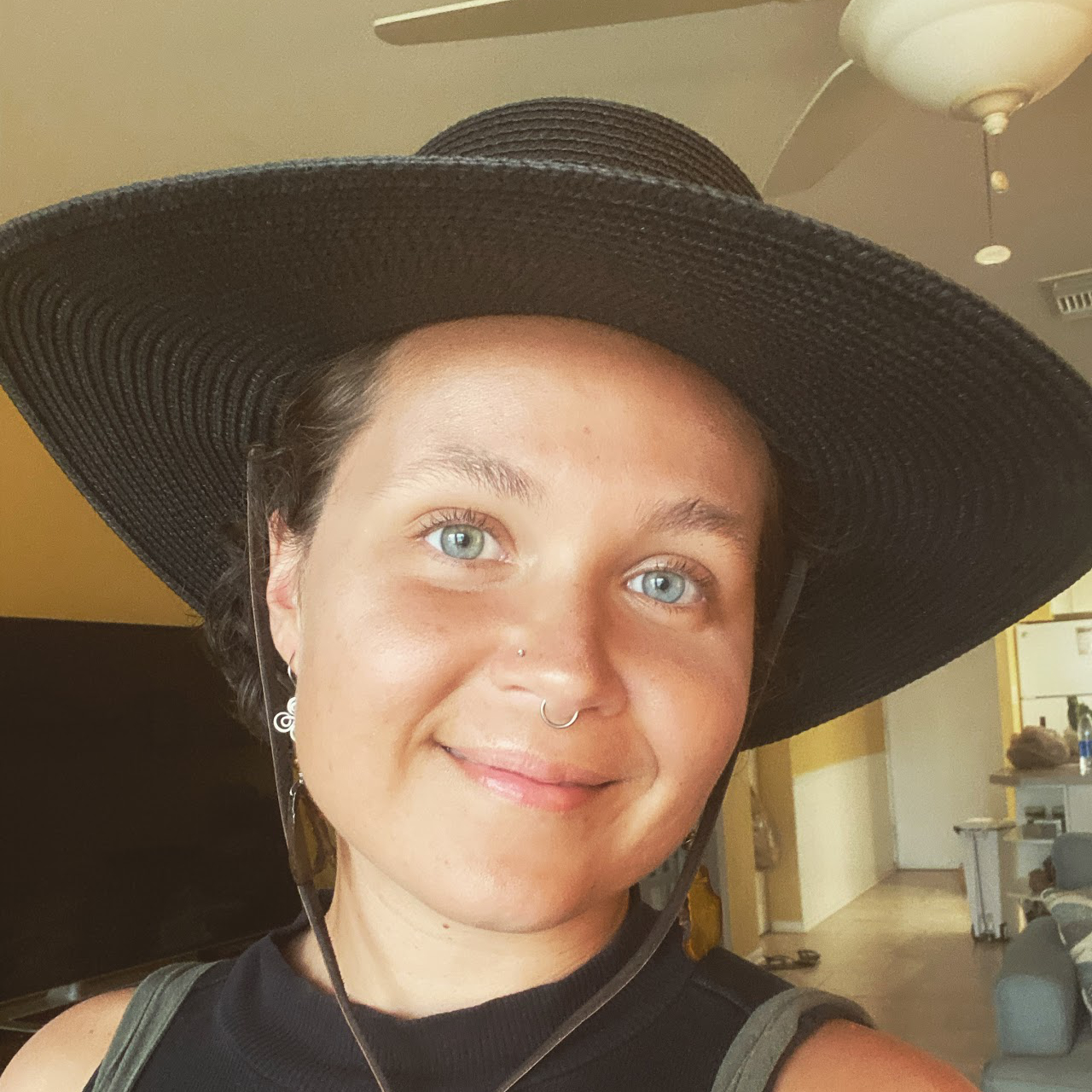 A young woman wearing a wide brimmed hat looks directly at the camera with peaceful a smile on her face.