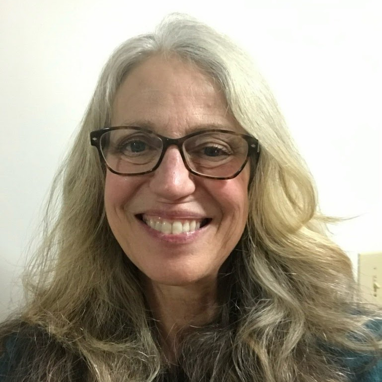 An older woman with silver hair, stylish glasses, and bright teeth looks directly into the camera