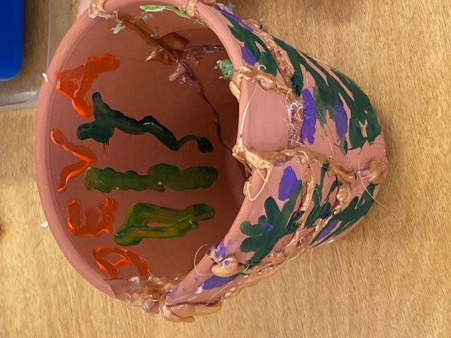 a pot that has been smashed and glued together with golden colored hot glue, and painted with purple flowers